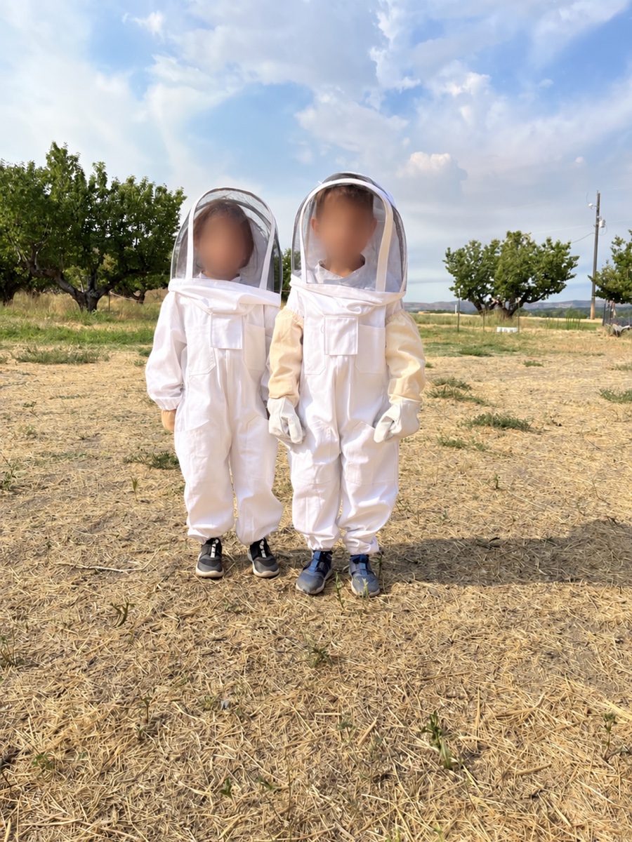 Pa’s grandchildren wearing beekeeping suits outdoors, with their faces blurred for privacy